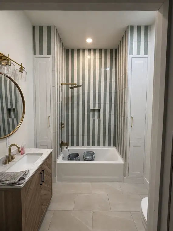 Finished bathroom with striped green tile, gold fixtures and built-in cabinets