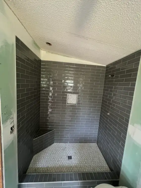 Gray subway tile walk-in shower with corner bench and niche